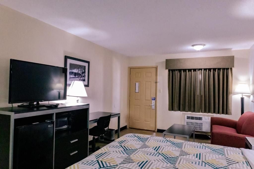 A hotel room with a bed, a desk, a television, a chair, a door, and a window with curtains.