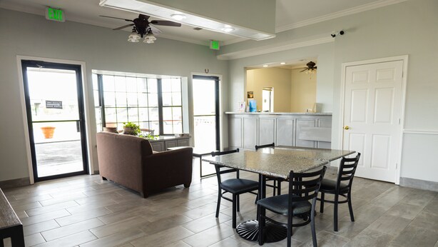 A spacious kitchen with a granite countertop, four chairs, and a ceiling fan.