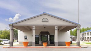 A building with a covered entrance, a number plaque, and two orange planters. - Motel 6 Nacogdoches TX (Nacogdoches)