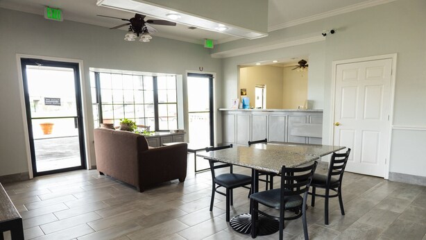 A spacious room with a large table and chairs, a sofa, and a kitchen area with cabinets and a countertop. - Motel 6 Nacogdoches TX (Nacogdoches)