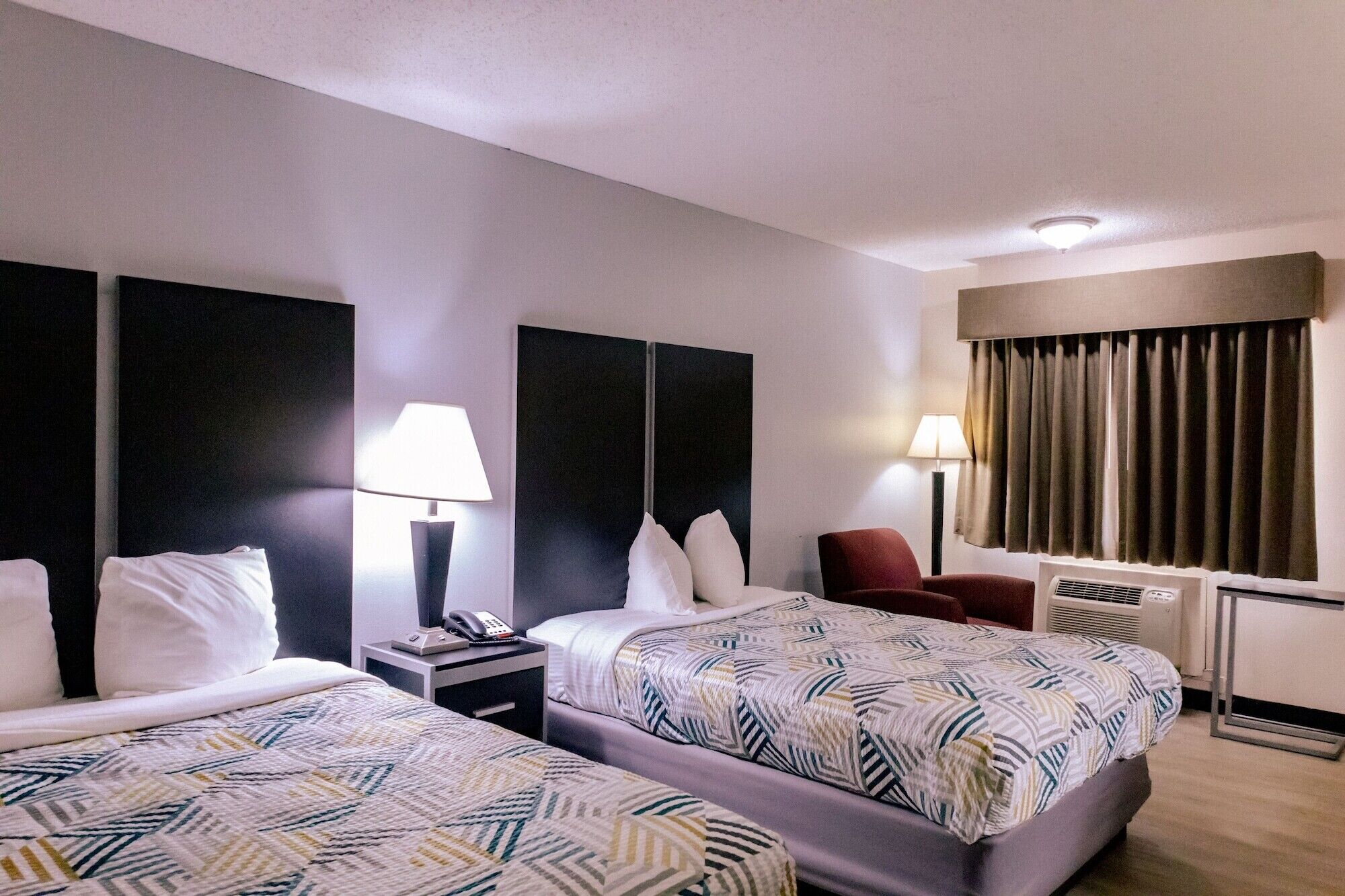 A hotel room with two beds, a desk, a chair, a phone, and a window with curtains.