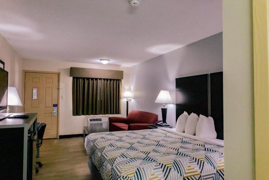 A hotel room with a bed, a desk, a chair, a TV, and a window with curtains.