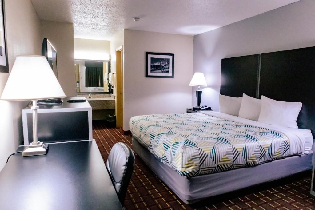 A hotel room with a bed, two bedside lamps, a desk with a lamp, a chair, a mirror, and a framed picture on the wall.