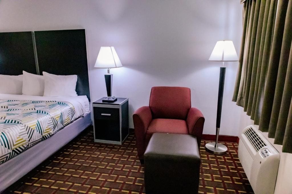 A hotel room with a bed, a desk, a chair, a table, and a heater.