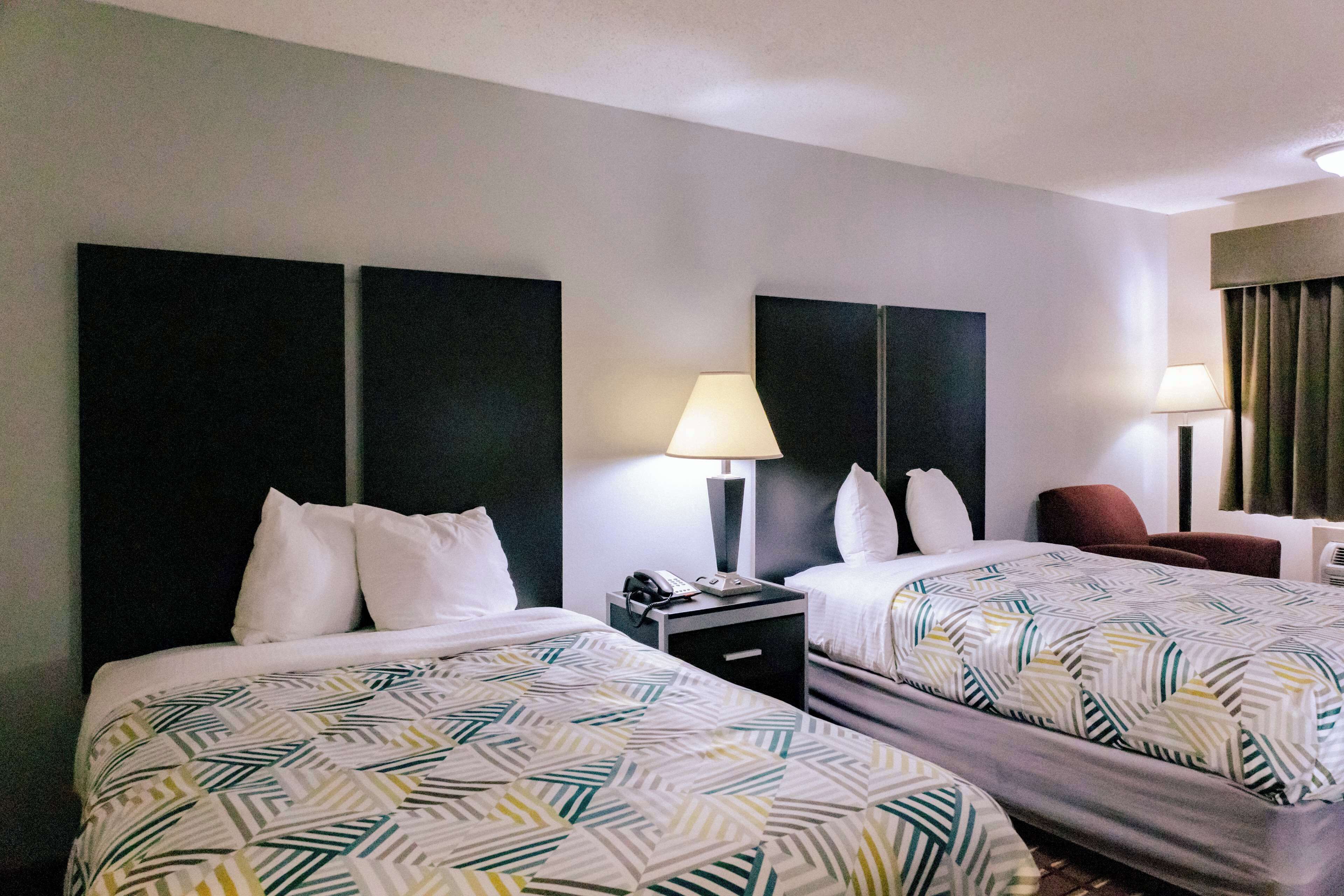 A hotel room with two beds, each with a patterned bedspread, a nightstand with a lamp, and a chair.
