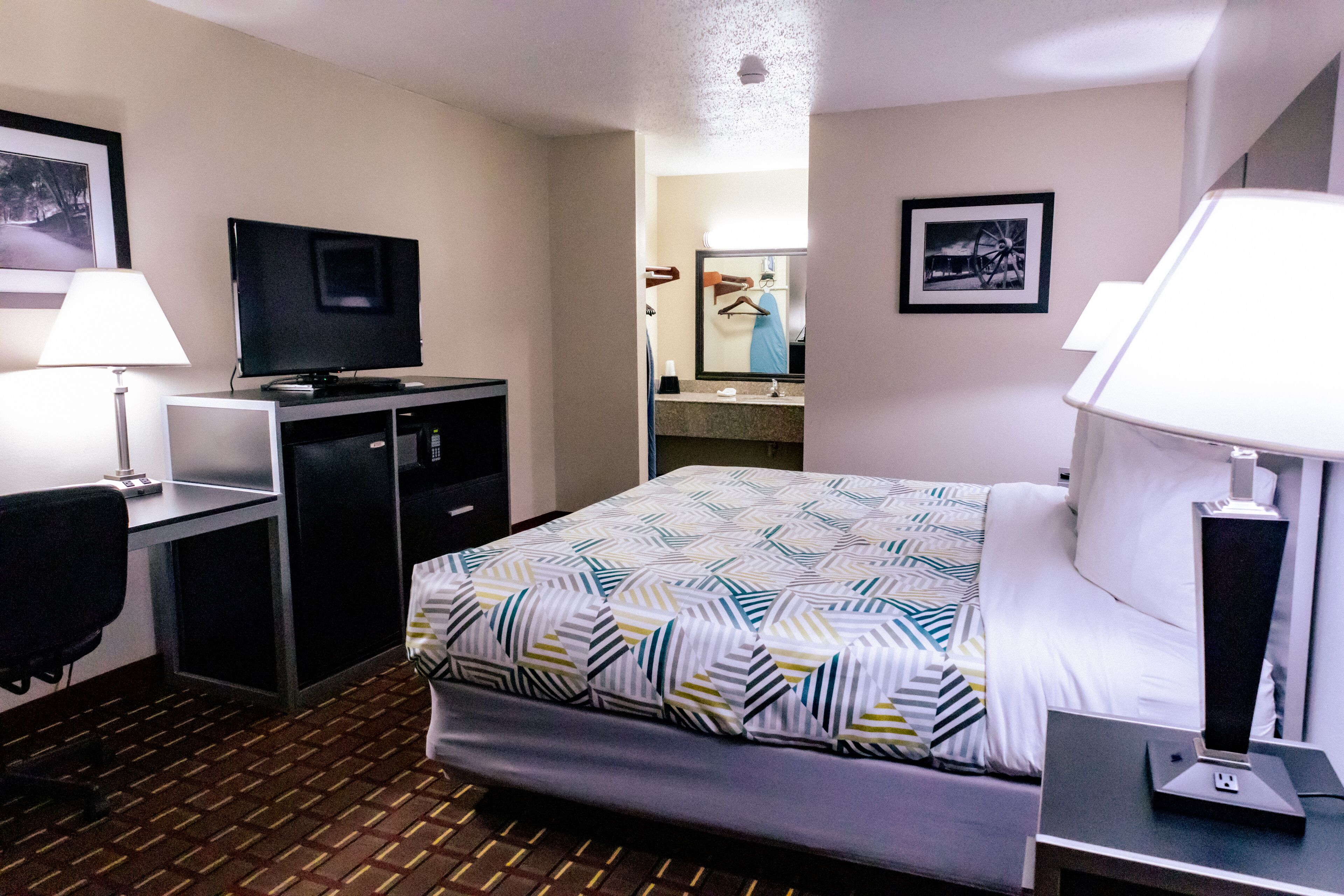 Une chambre d’hôtel avec un lit, un bureau, une télévision et un miroir.