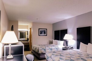Una habitación de hotel con dos camas, un escritorio, una silla, una lámpara y un cuadro en la pared.