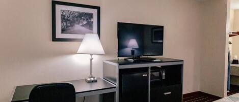 A hotel room with a desk, chair, television, and a bed with patterned bedding.