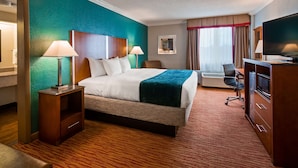 Una habitación de hotel con una cama, lámparas de noche, un escritorio con una silla, un televisor y un microondas.
