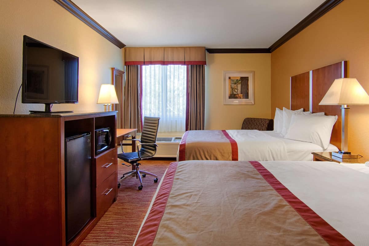 Habitación de hotel con escritorio, dos camas, televisor y ventana con cortinas.