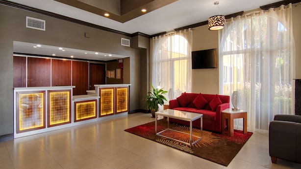 Un moderno hall de hotel con un mostrador de recepción, un sofá rojo y un ventanal con cortinas.