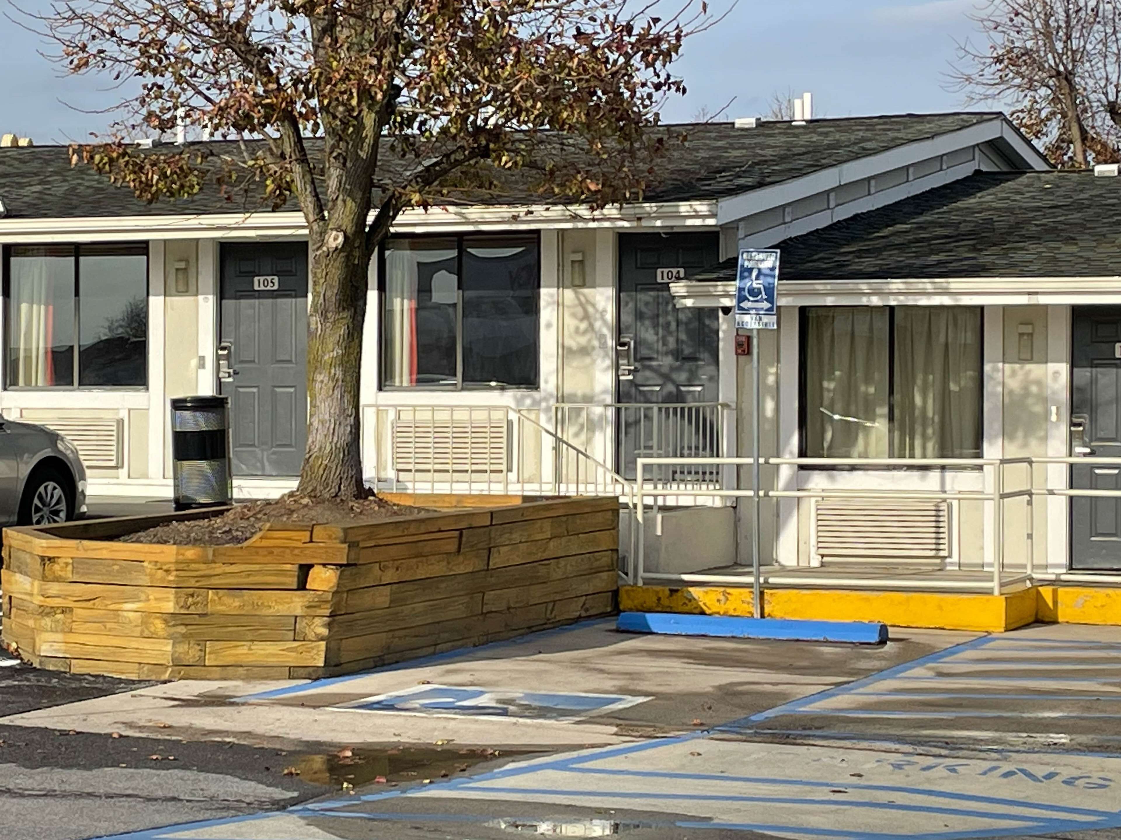 A motel with a parking lot, marked handicap parking, and a tree in front.