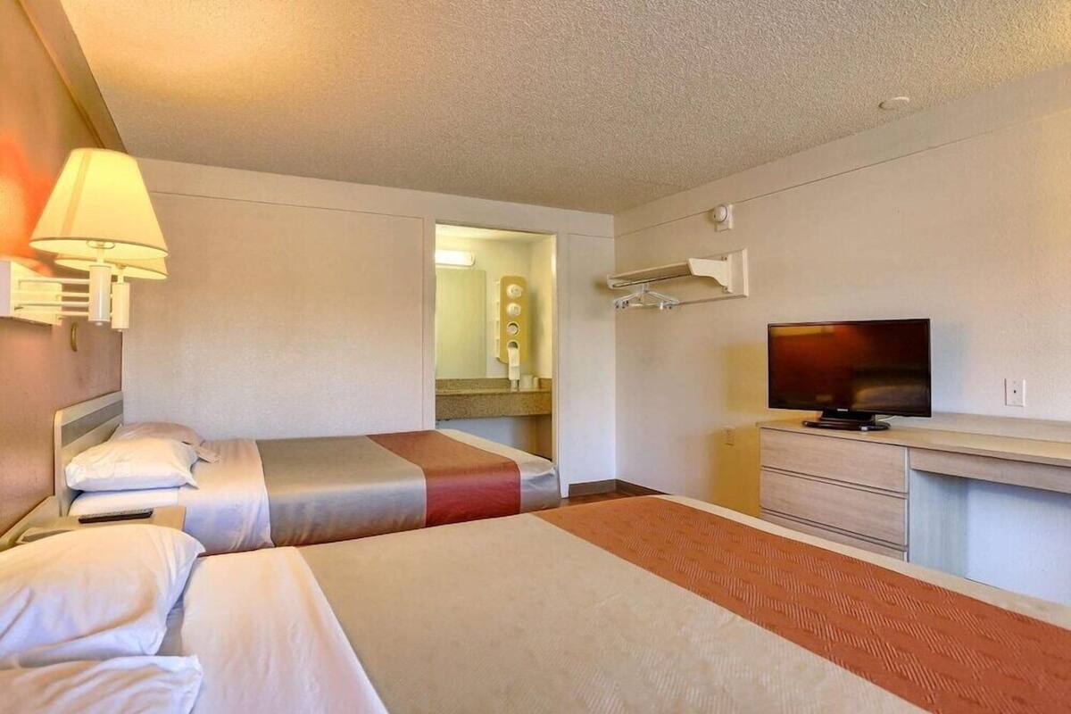 Ein Hotelzimmer mit zwei Betten, einem Fernseher, einem Schreibtisch und einem Spiegel.