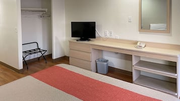 A hotel room with a wooden desk, a television, a telephone, a trash bin, and a closet with a hanging rack.