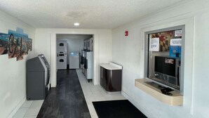 Ein sauberes, modernes Entree mit einem schwarz-weißen Fliesenboden, einem Kühlschrank, einer Waschmaschine und einem an der Wand befestigten Fernseher.