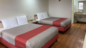 Ein Hotelzimmer mit zwei Betten, Holzboden, einem kleinen Nachttisch und einem durchgegangenes Badezimmer.