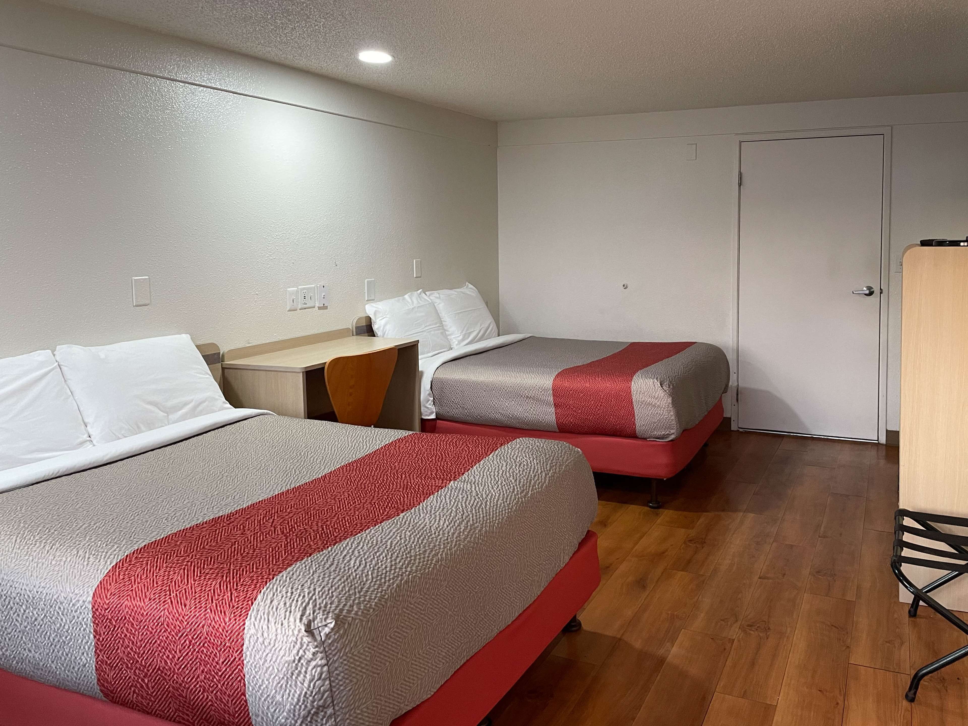 Une chambre d’hôtel avec deux lits, une table de chevet en bois, une porte blanche et une armoire.