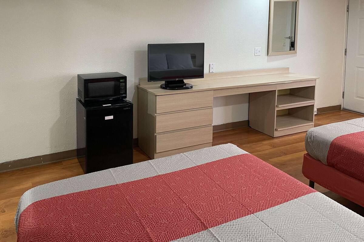 Ein Hotelzimmer mit Schreibtisch, Fernseher, Minibar und zwei Betten mit gemusterten Bettbezügen.