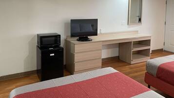 A hotel room with a desk, a television, a minibar, and two beds with patterned bedding.