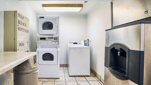 Ein Waschraum mit gestapelten Waschmaschinen und Trocknern, einer Arbeitsplatte mit Mülleimer und einem Wasserspender.