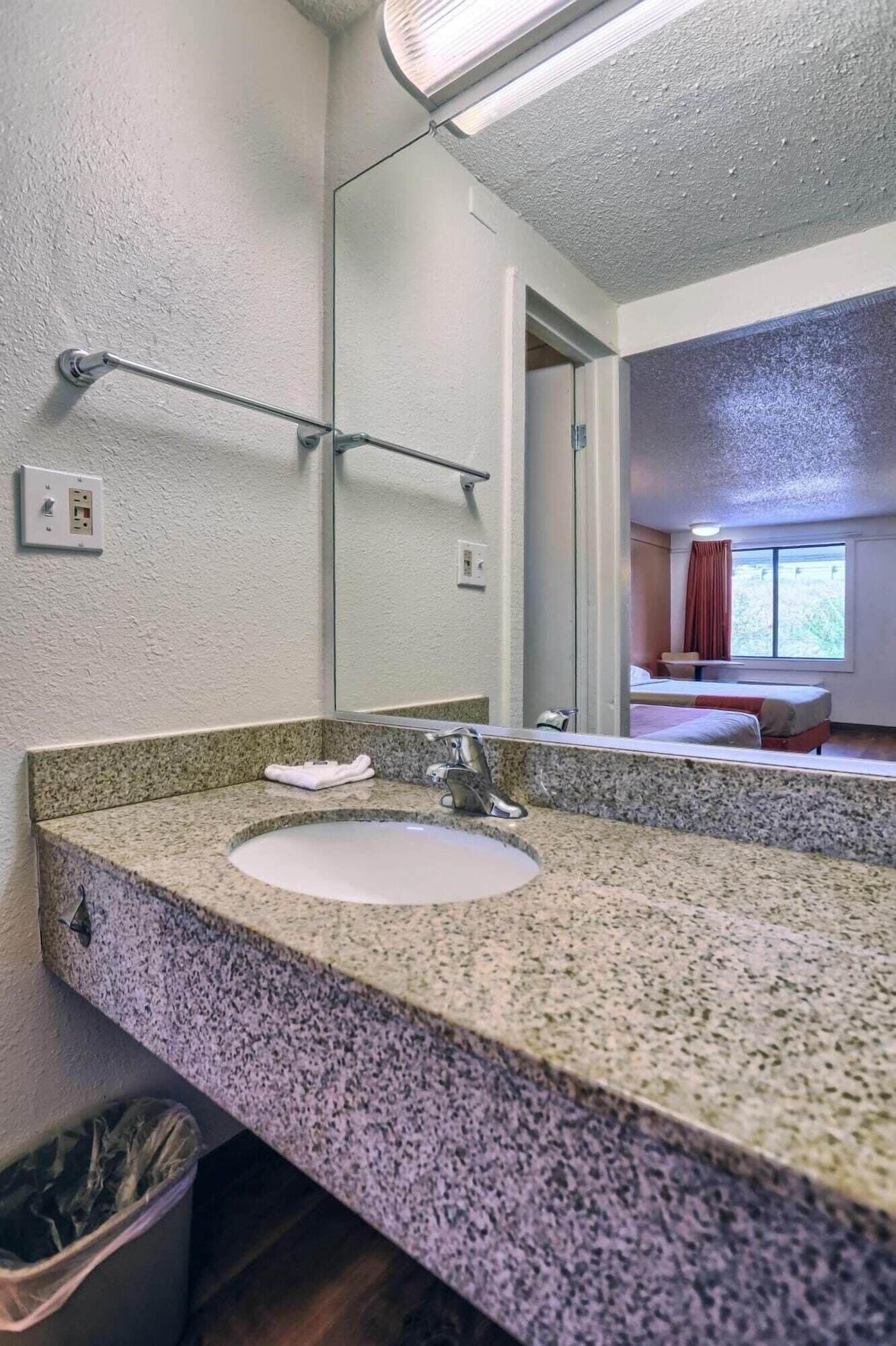 A bathroom with a granite countertop sink, a mirror, and a towel rack.