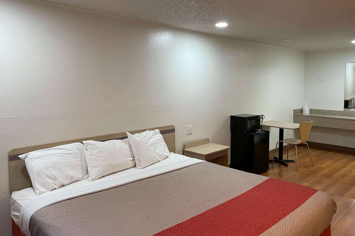 Ein Hotelzimmer mit Bett, Schreibtisch, Stuhl, Mikrowelle und kleinem Kühlschrank.
