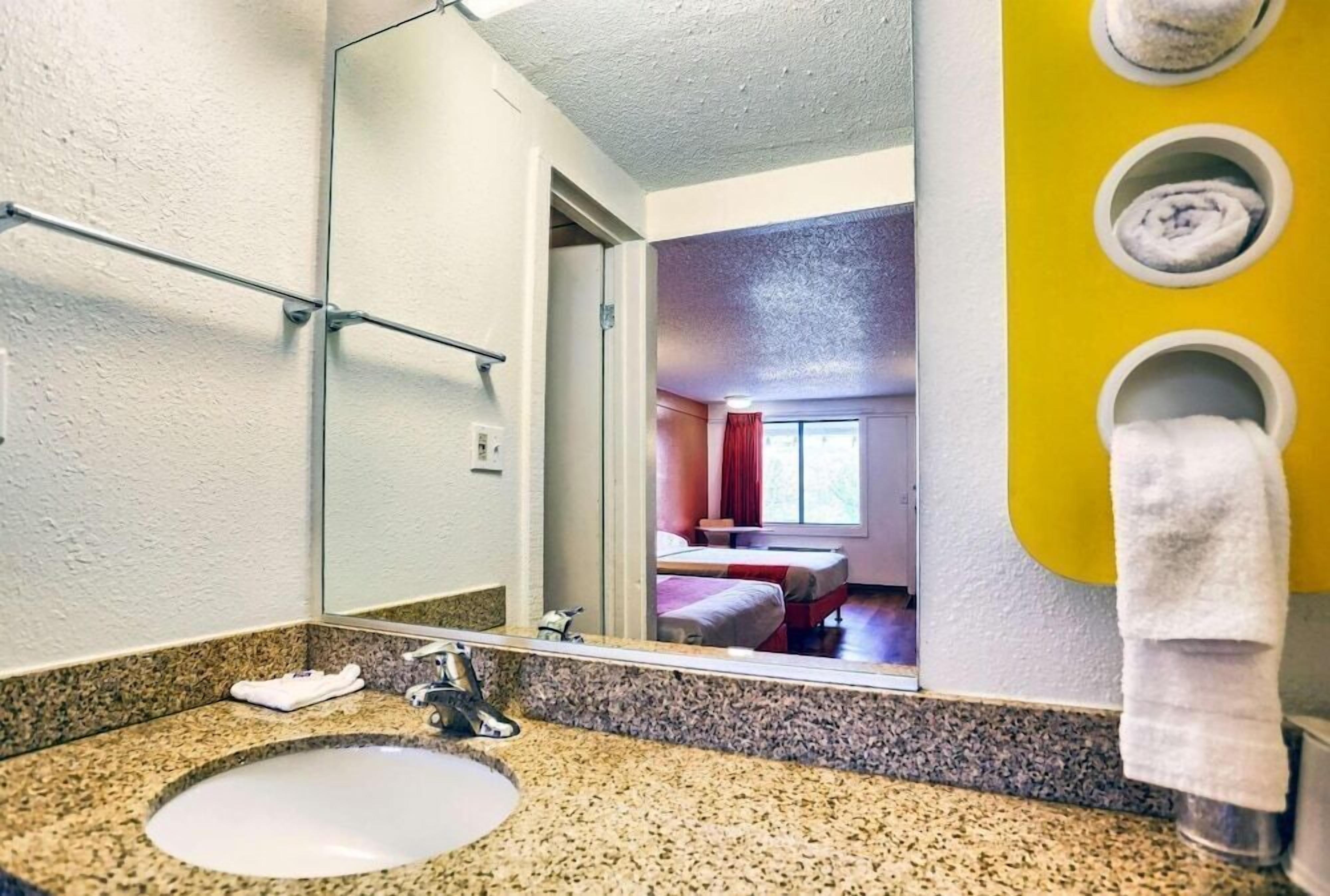 Baño de hotel con lavamanos de encimera de granito, espejo y toallero.