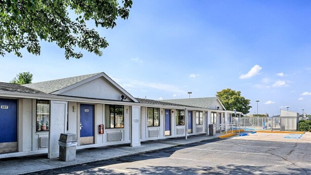 Motelzimmer mit individuellen Türen, ein Parkplatz und ein kleines Gebäude im Hintergrund.