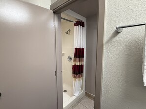A bathroom with a shower, a white door, and a towel rack. - Red Roof Inn Austin - Round Rock (Round Rock)