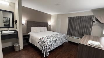 A hotel room with a bed, a bedside table, a mirror, a sink, and a window with curtains.