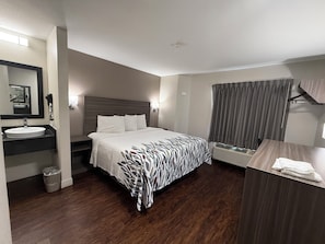 A hotel room with a bed, a bedside table, a mirror, a sink, and a window with curtains. - Red Roof Inn Austin - Round Rock (Round Rock)