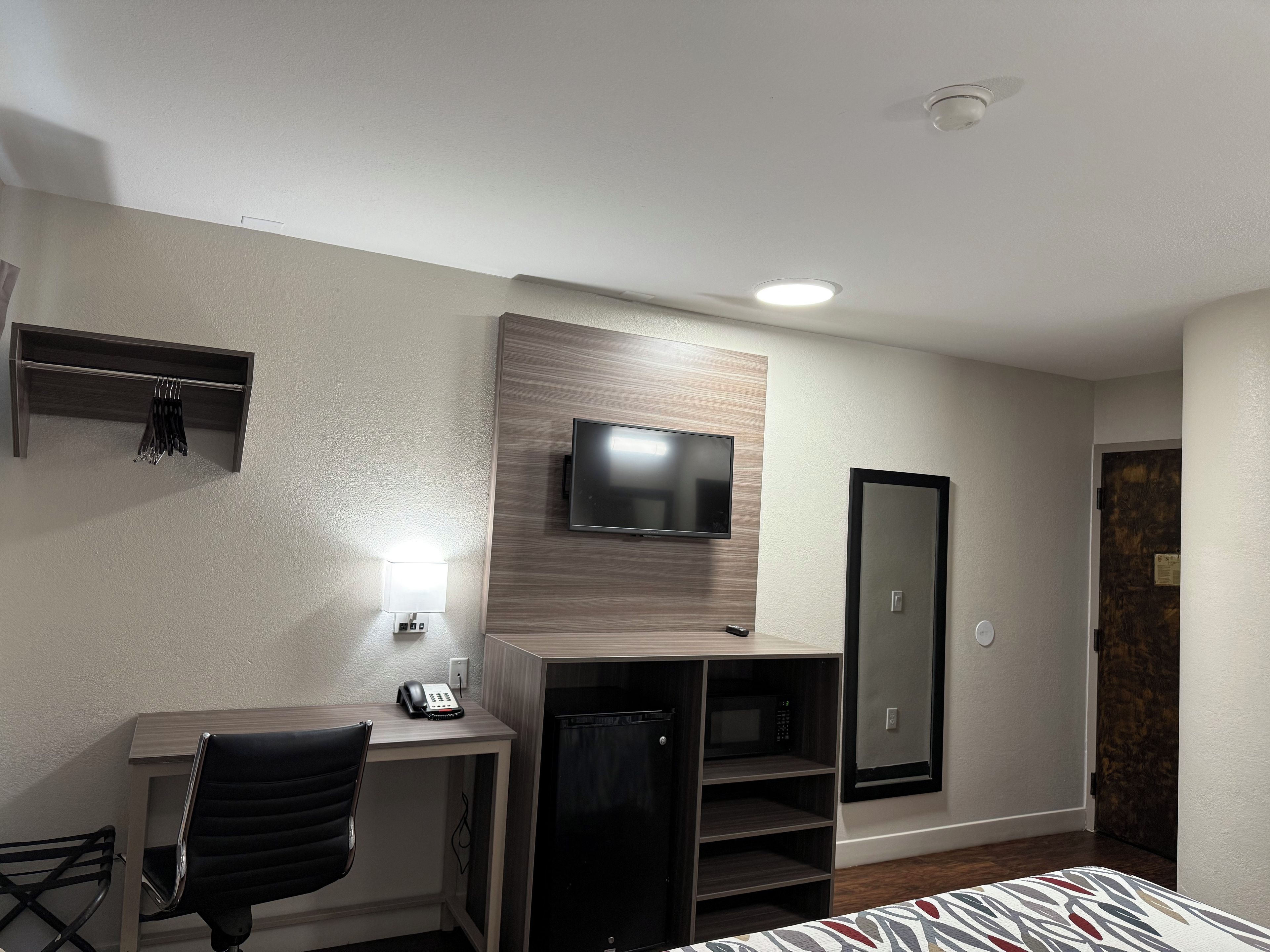 A hotel room with a desk, chair, television, and a wardrobe.