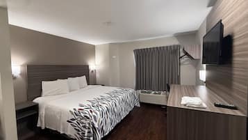 Habitación de hotel con una cama grande, un escritorio, un televisor de pantalla plana y una ventana con cortinas.