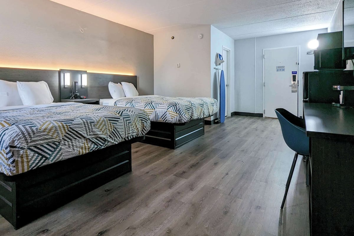 A hotel room with two beds, a desk, and a chair.