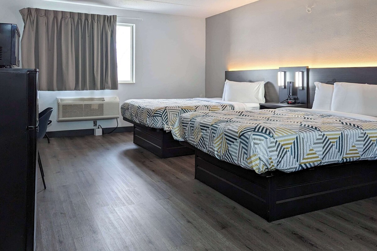 A hotel room with two beds, a desk, a chair, a TV, and a window with curtains.