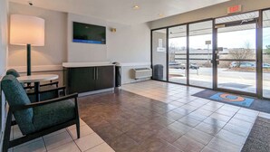 A reception area with a TV, a counter, a chair, and a view of the parking lot. - Motel 6 Danvers, MA - Boston North (Danvers)