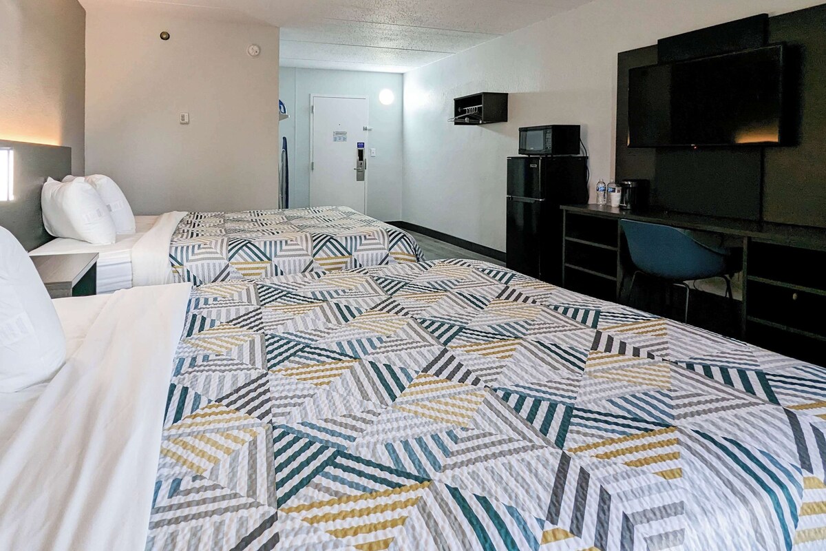 A hotel room with two beds, a desk, a chair, a TV, and a minibar.