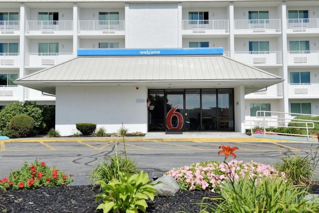 A hotel entrance with a 'welcome' sign, a large number '6' above the door, and a parking lot with marked spaces.