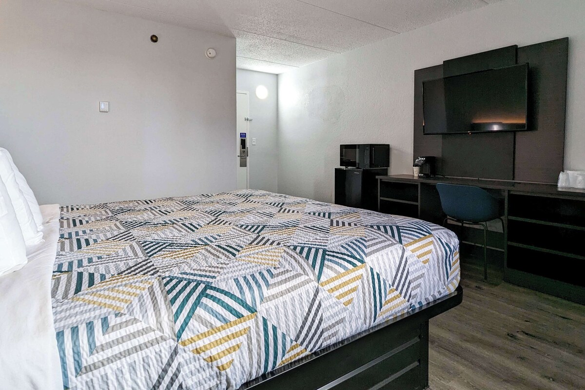 A hotel room with a bed, a desk, a chair, a TV, and a small kitchenette.