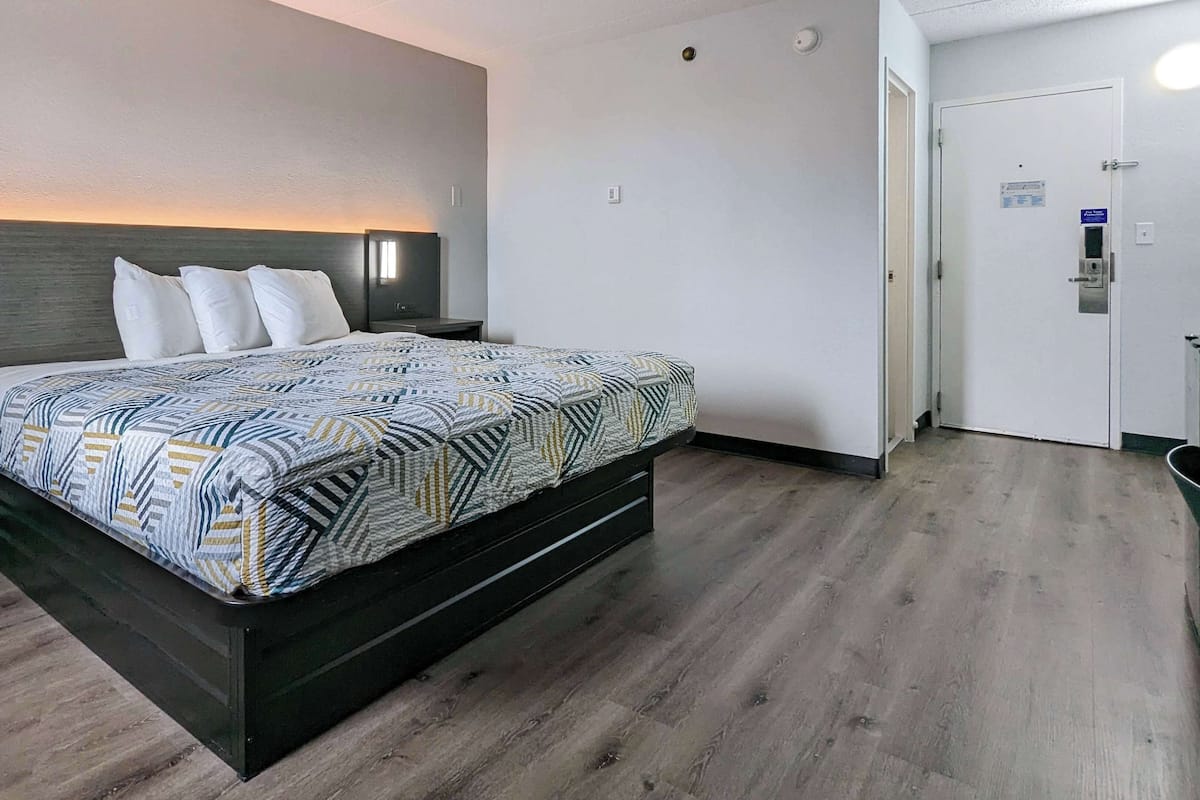 A modern hotel room with a large bed, a nightstand, a bedside table, and a wall-mounted lamp.