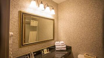 Une salle de bain avec un grand miroir, trois appliques murales, un plan de toilette noir, un lavabo et des toilettes.