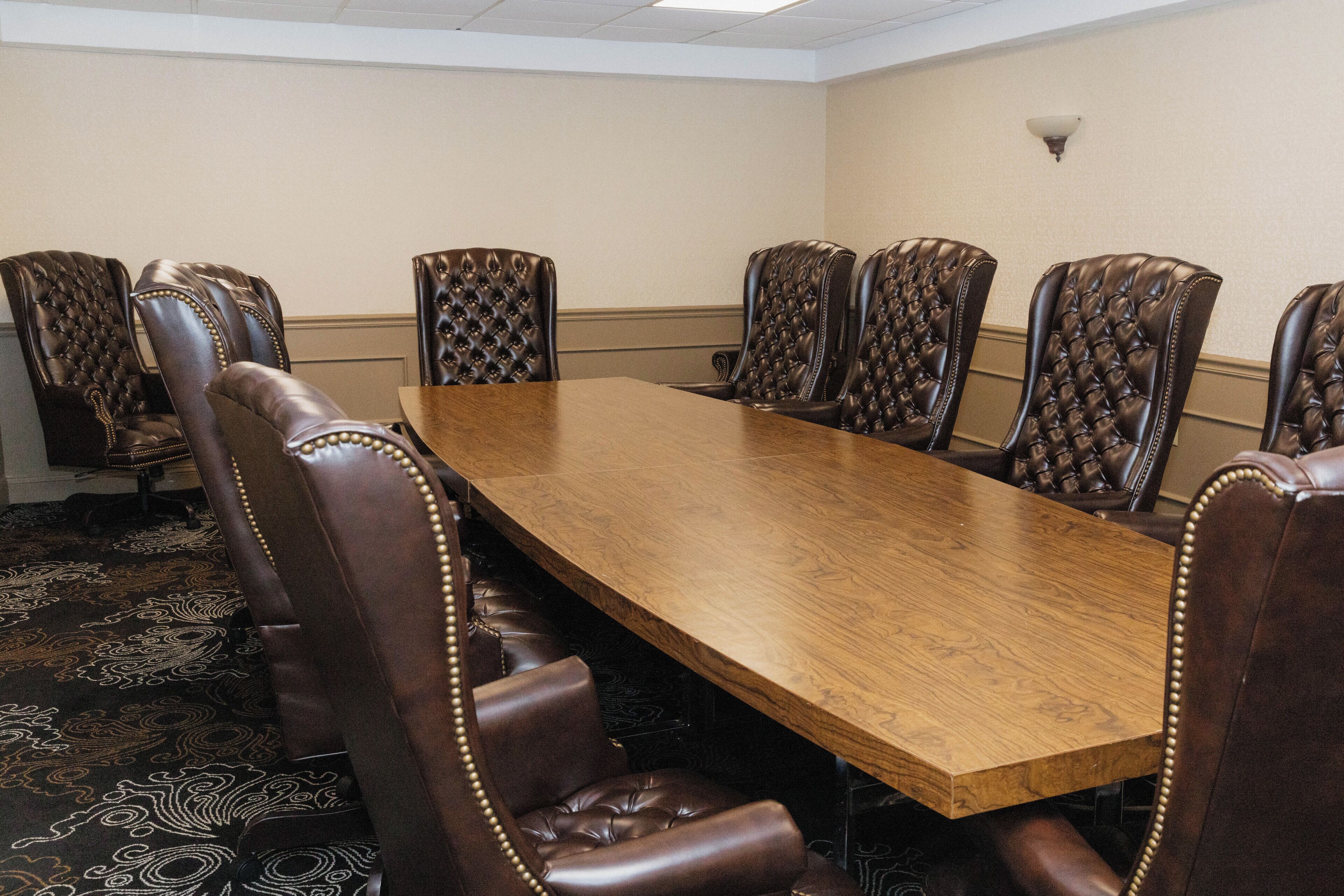 Una sala de conferencias con una larga mesa de madera y seis sillas de cuero con respaldo alto.