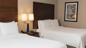 A hotel room with two beds, a nightstand with a lamp, and a framed picture on the wall.
