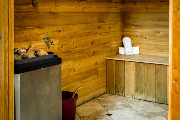 A wooden cabin interior with a wooden wall, a sink, a small trash bin, and a towel rack.
