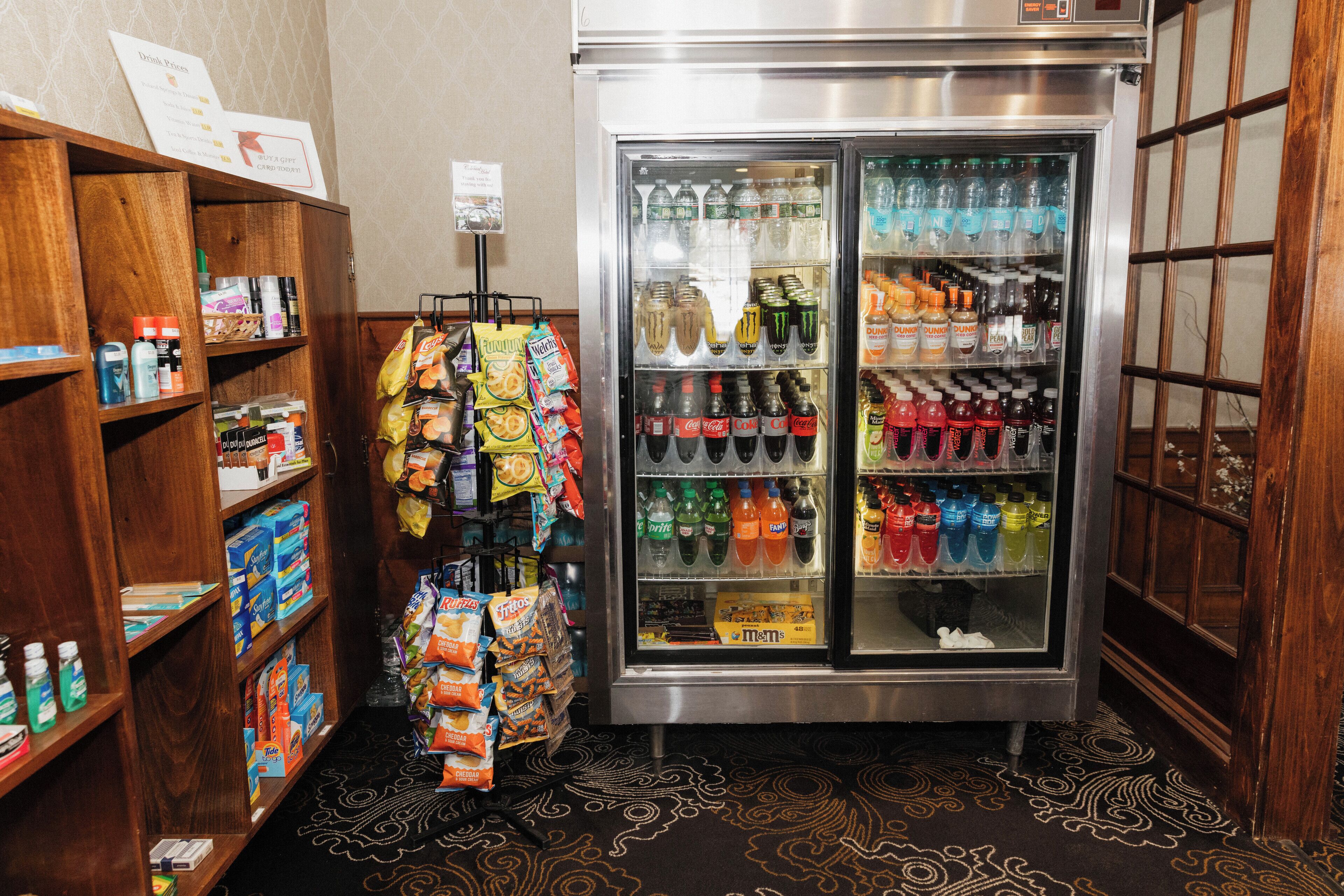 A vending machine with various drinks and snacks, surrounded by wooden shelves stocked with toiletries and other items.