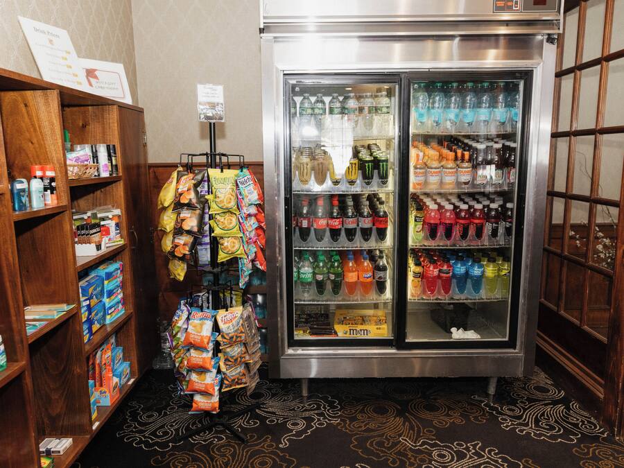 A vending machine with various drinks and snacks, surrounded by wooden shelves stocked with toiletries and other items.