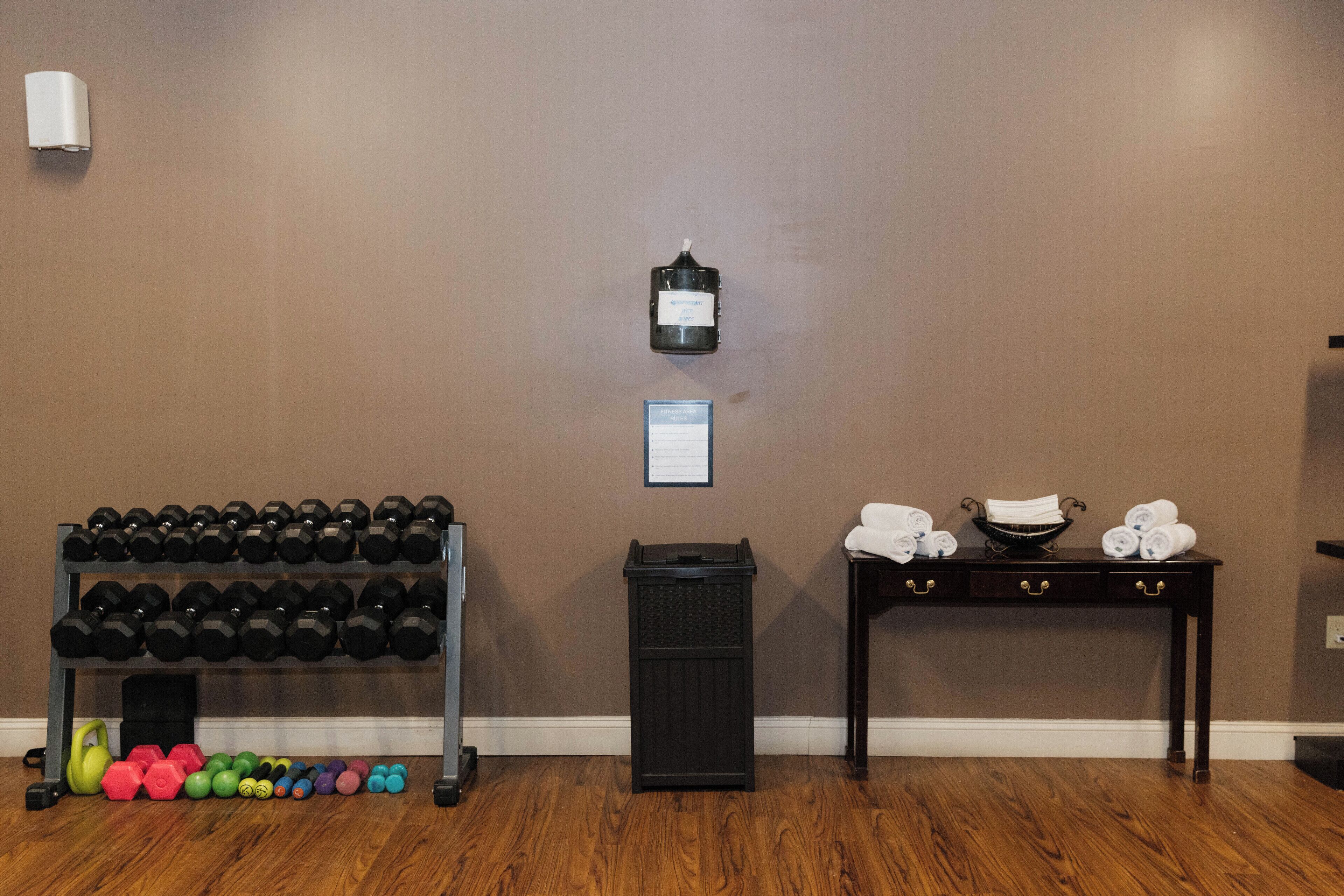 A gym with a rack of dumbbells, kettlebells, and a trash bin.