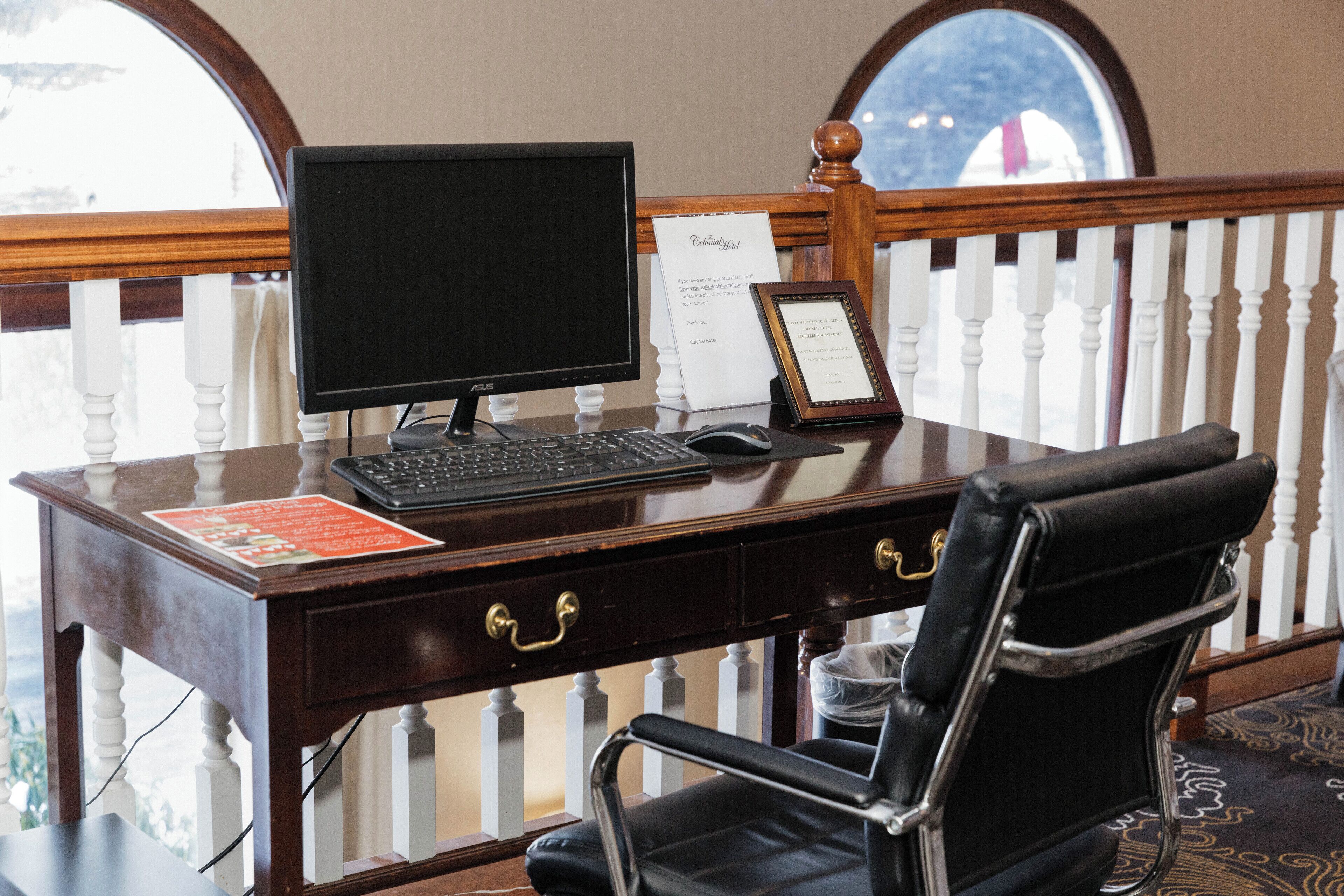 A wooden desk with a computer, keyboard, and mouse. There is a framed certificate on the desk. A black leather chair is in front of the desk.