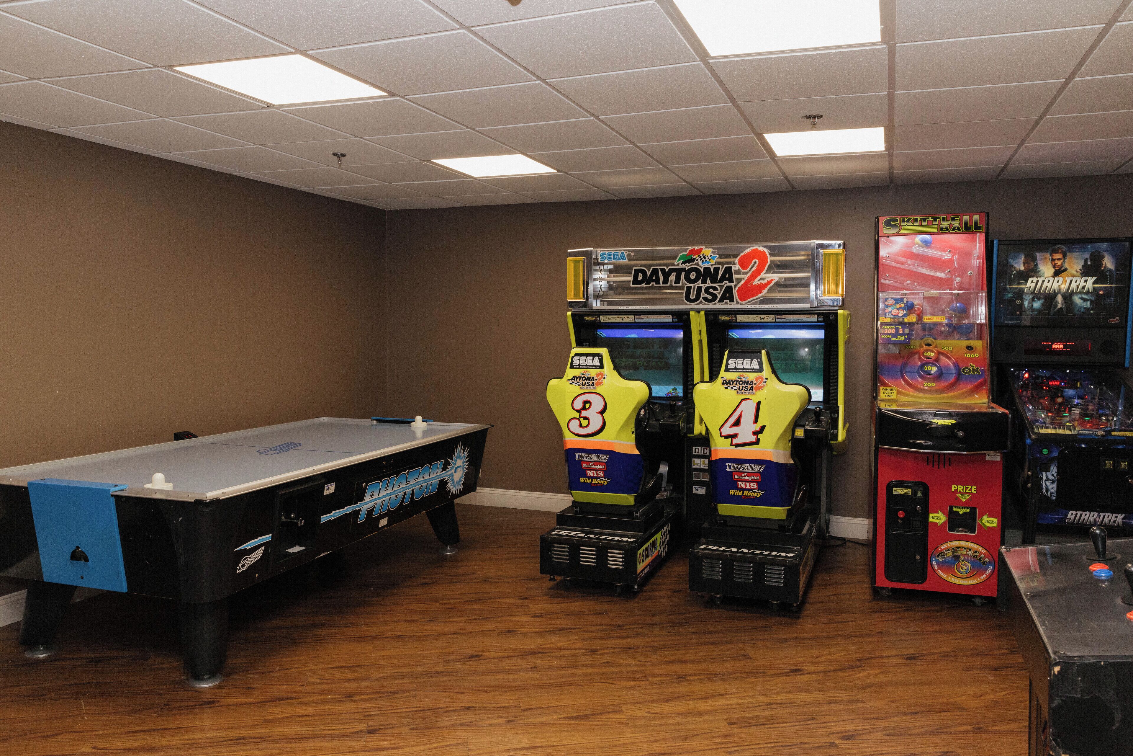 Una sala con mesa de billar, dos máquinas recreativas con la etiqueta 'Daytona USA' y una máquina recreativa 'Spaceball'.