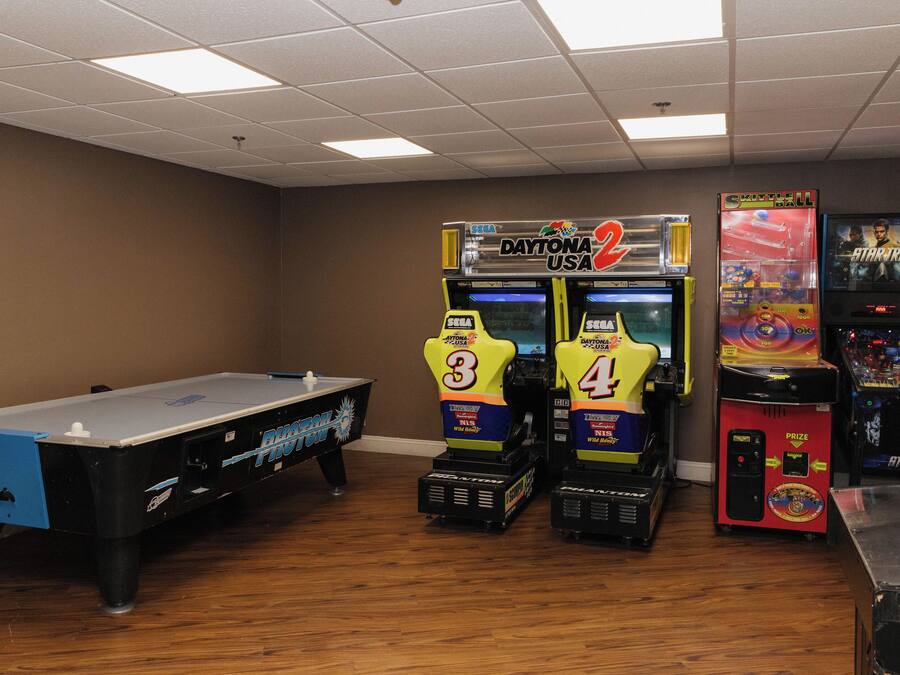 Una sala con mesa de billar, dos máquinas recreativas con la etiqueta 'Daytona USA' y una máquina recreativa 'Spaceball'.
